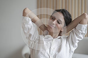 Young happy Spanish woman with closed eyes dreaming, holding hands behind head