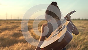 Close-up Young hipster girl holding guitar in hand and walking in the wheat field. Woman with acoustic instrument