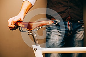 Close-up of young hipster man holding hands on his bicycle while standing indoors. Warm color.