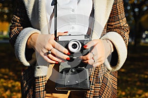 Close-up young hipster woman holding retro film camera, taking photo outdoors. Girl photographer and vintage camera, hobby