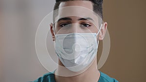 Close up young hispanic man doctor arabian male face in medical mask with dark eyes looking at camera confident adult