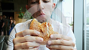 Close-up of young hungry man eats hamburger in a cafe, fast food restaurant