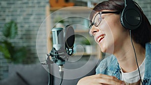 Close-up of young lady in headphones speaking in microphone smiling in studio