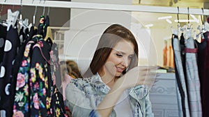 Close-up of young lady shopping for clothes, going through colourful garments on rails, touching and moving them. Trendy