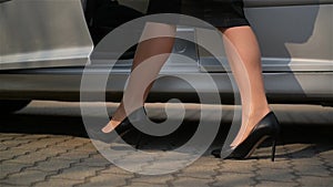 Close-Up Of Young Lady In Spotted Dress Getting Out Of Car And Walks By Road. Low Angle View With Focus On Woman`s Legs.