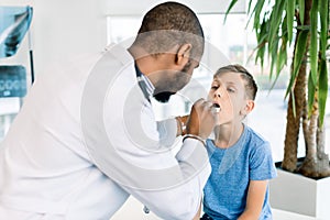 Close-up Of A Young male African Doctor Checking His Patient`s Boy Throat In Clinic