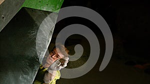 CLOSE UP: Young male climber wearing glasses reaches up to grab a black volume.