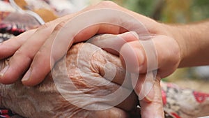 Close up of young male hand comforting an elderly arms of old woman outdoor. Grandson and grandmother spending time