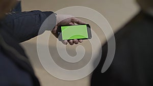 Close up of young male hands holding modern smartphone with green touch screen. Man`s hand shows mobile smartphone with