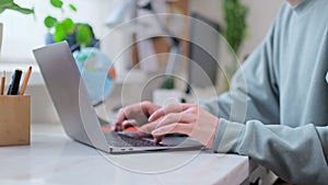 Close-up of young male hands typing on laptop, in home interior