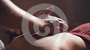 Close-up Young male massage therapist does back massage to a woman with a tattoo in a massage room with dim lights on