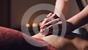 Close-up Young male massage therapist does back massage to a woman with a tattoo in a massage room with dim lights on