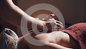 Close-up Young male massage therapist does back massage to a woman with a tattoo in a massage room with dim lights on