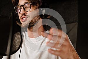 Close up young male singer in headphones emotionally singing in sound recording studio