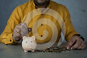 Close up young male in yellow shirt putting coin in piggy bank. Saving money for household payments