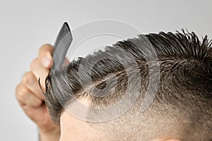 Close up young man combing his hair with a plastic comb. Styling hair after barbershop.