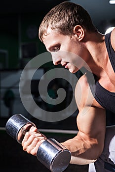 Close-up of young man doing concentration curls with dumbbell