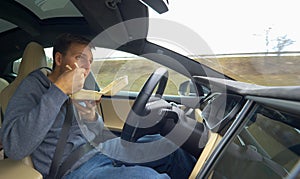 CLOSE UP: Young man eating Chinese food while driving in his high tech car.