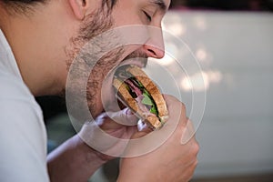 Close up of a young man eating a pastrami sandwich.