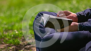 Close up of young man holding a Bible in his hands sitting in park.