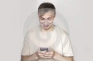 Close up of a young man leaning against a grey wall using mobile phone. Portrait of a happy business man holding a smartphone. Man