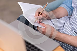 Close up of young man making notes by the laptop.