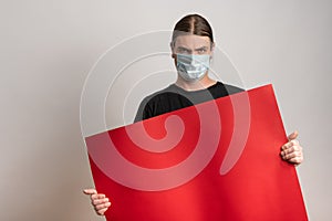 Close up of a young man with protective mask against virus epidemy is holding an empty red cardboard against white