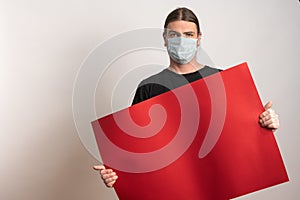 Close up of a young man with protective mask against virus epidemy is holding an empty red cardboard against white photo