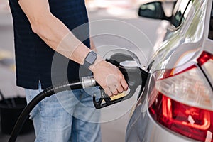 Close-up of young man refuelling a car at a petrol station. Middle selection of human hand hold fuel pump