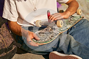 Close up of young man repairing his skateboard in the skate park. Extreme sport concept