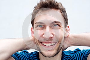Close up young man smiling with hands behind head by white background