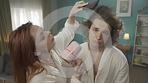 Close up of a young man standing in a room holding a hair dryer. Looks at him uncertainly, distrustful. He is drying his