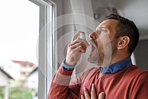 Close-up of young man in suffocation inhaling through asthma pump by window at home