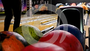 Close-up of young man taking bowling balls from the rack. Media. Competitive cheerful friends playing bowling together