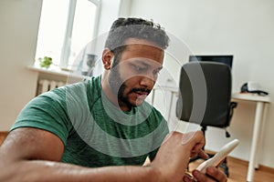 Close up of young man using smartphone app while having morning workout at home. Freshman relaxing after training