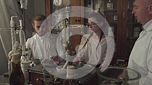 Close-up of young man and woman listening to mature pharmacist in white robe and holding test tubes. Two new workers in