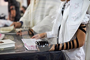 Close up, young men reading Jewish prayer and a hand with tefillin and talit.Selective focus