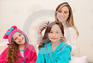 Close up of young mom brussing the hair of her little daugher who is wearing a blue bathtowel while her other curly girl