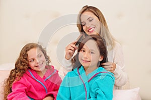 Close up of young mom brussing the hair of her little daugher who is wearing a blue bathtowel while her other curly girl