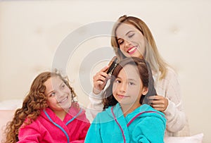 Close up of young mom brussing the hair of her little daugher who is wearing a blue bathtowel while her other curly girl