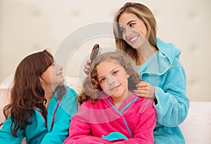 Close up of young mom brussing the hair of her little daugher who is wearing a blue bathtowel while her other curly girl