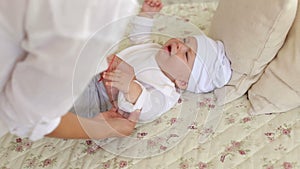 Close-up of a young mom dressing her newborn baby on the bed in the bedroom.