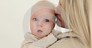 Close-up of a young mother, blonde, holding a newborn baby in her arms indoors, kissing him. The woman smiles. Parenting