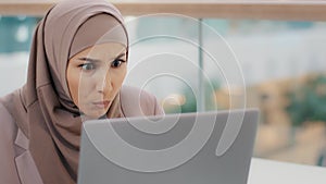 Close-up young muslim woman user looks attentively into laptop surprised arab businesswoman in hijab reads good news