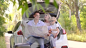 Close-up of young parents and a small boy traveling by car, dad holding a map.