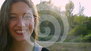 Close-up of young pretty girl looking at camera and smiling with copy space. Slow motion with sun in background