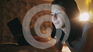 Close-up of young pretty woman using tablet computer at night time lying in bed at home