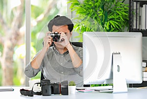 Close-up of a young professional photographer sitting in the office, hand holding a retro camera, taking pictures to test the