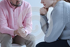 Close-up of a young sad woman sharing her grief with a psychotherapy specialist during an individual counseling meeting.