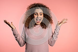 Close up of young scared curly girl shouting  over pink background. Stressed and depressed woman.